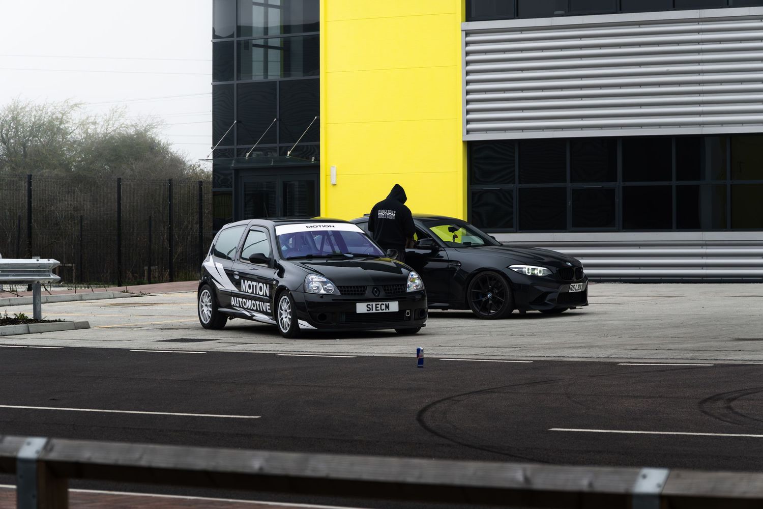 Motion Automotive Renault Clio and black Mercedes-Benz C63 AMG at industrial car park location.
