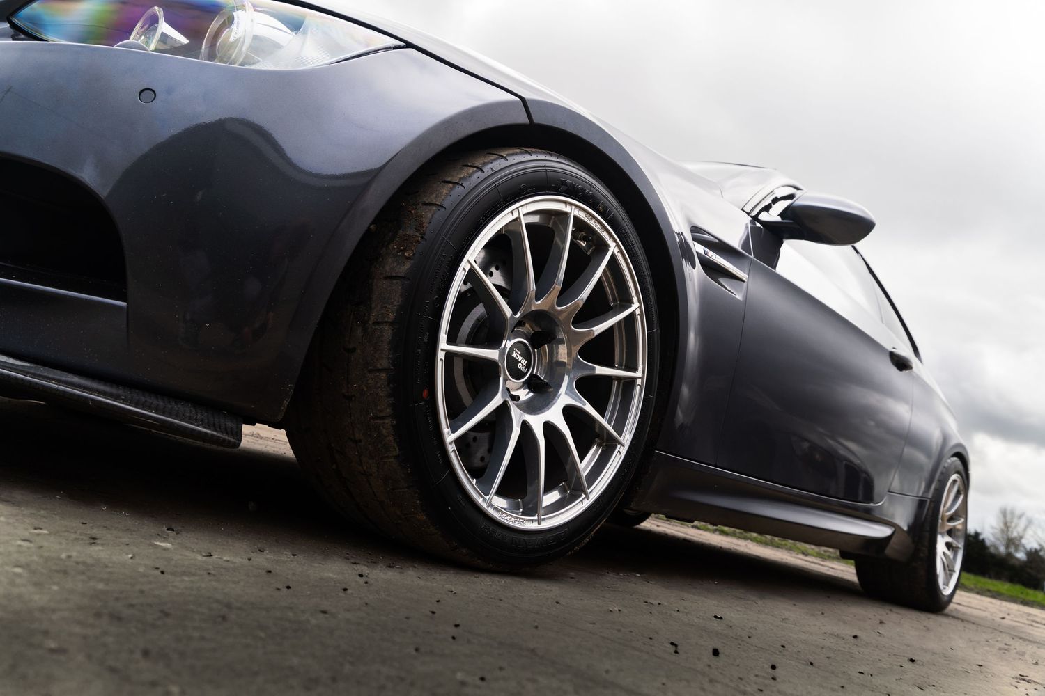 Close-up of a multi-spoke alloy wheel on a lowered gray BMW M3 E92 under cloudy skies.