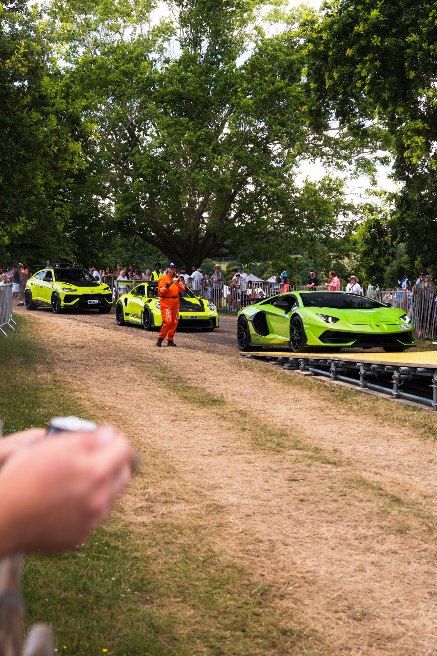 Three neon green Lamborghini supercars lined up at Goodwood Festival of Speed with crowds watching.