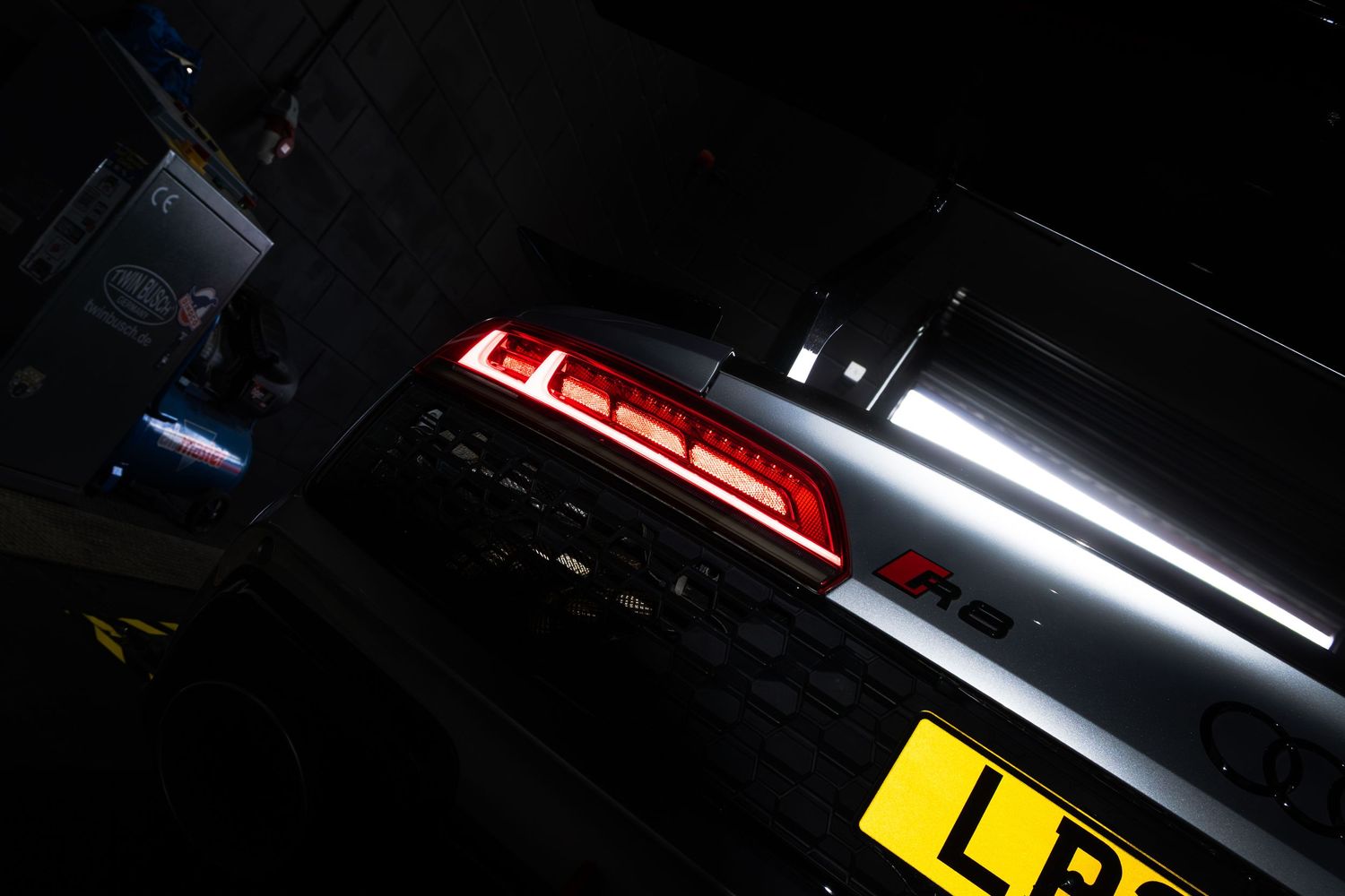 Close-up of a glowing red LED tail light on a silver car with a yellow UK number plate.