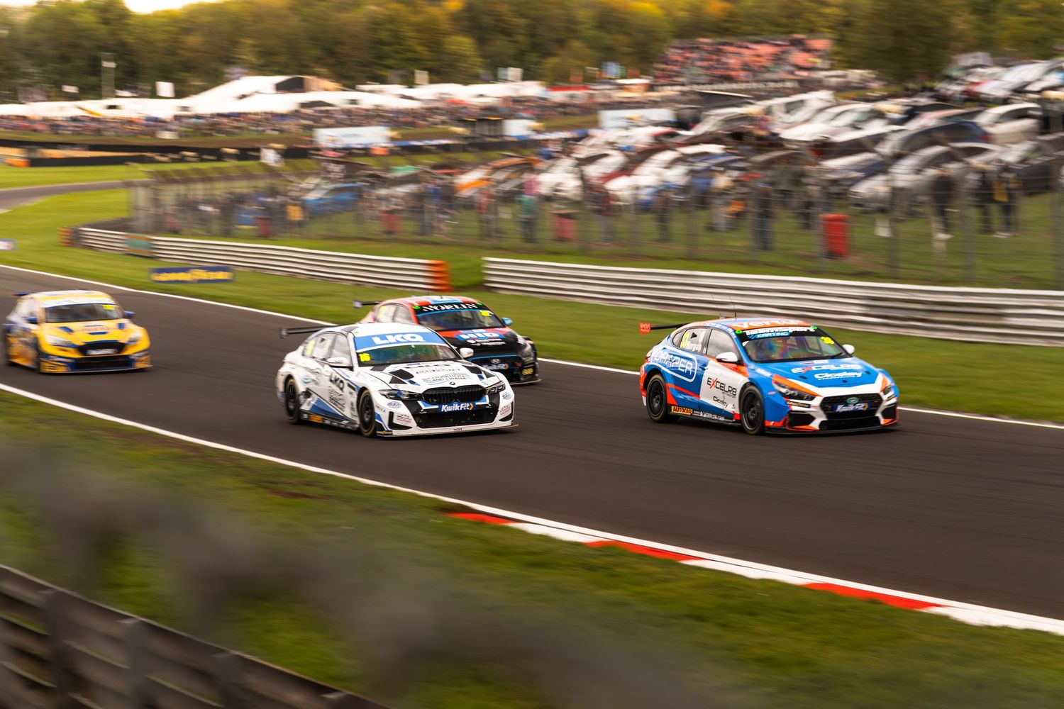 Three touring cars battle side by side through a corner at a British circuit race event.