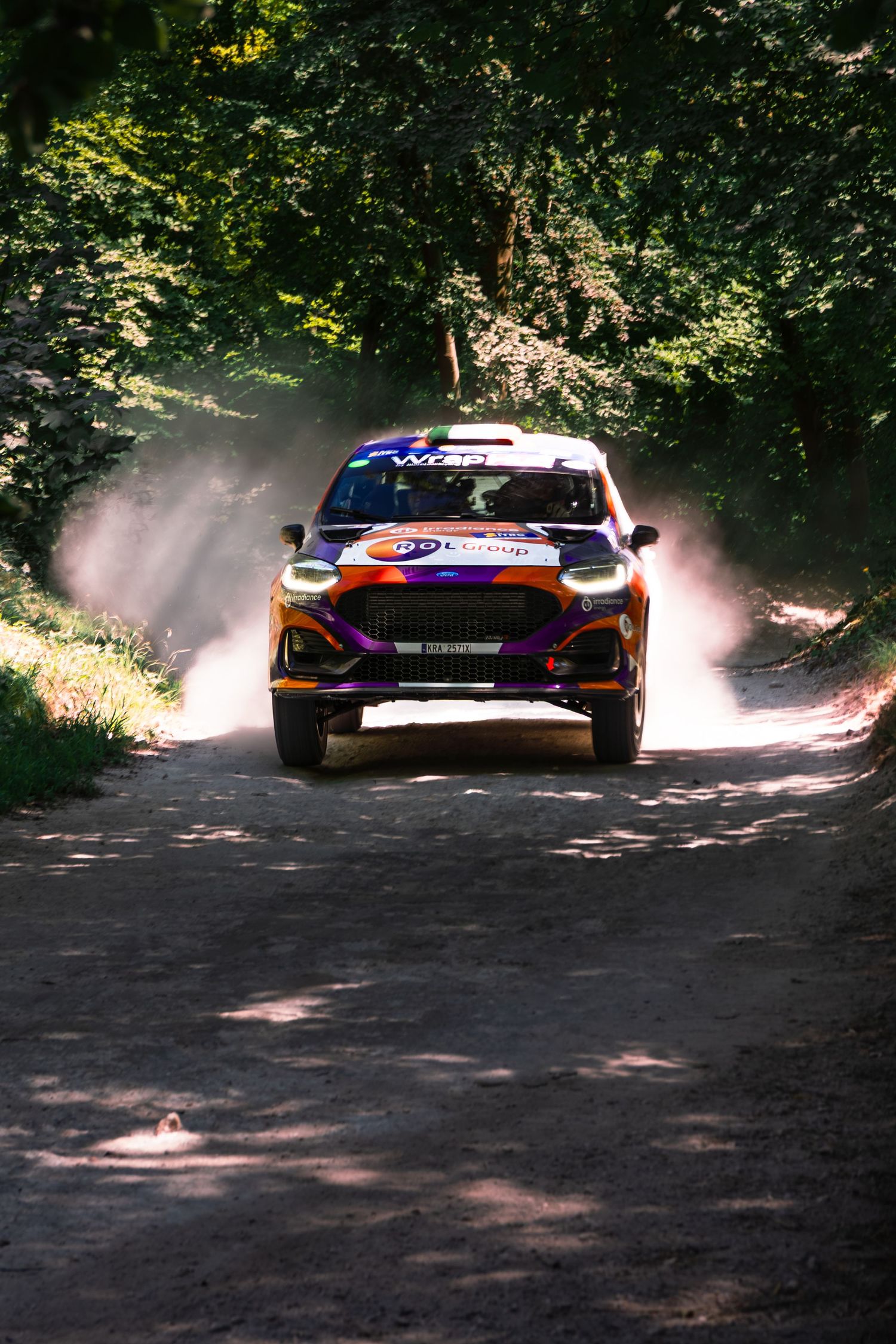 Rally car racing on dusty forest road, kicking up dust clouds during competitive off-road rally event.