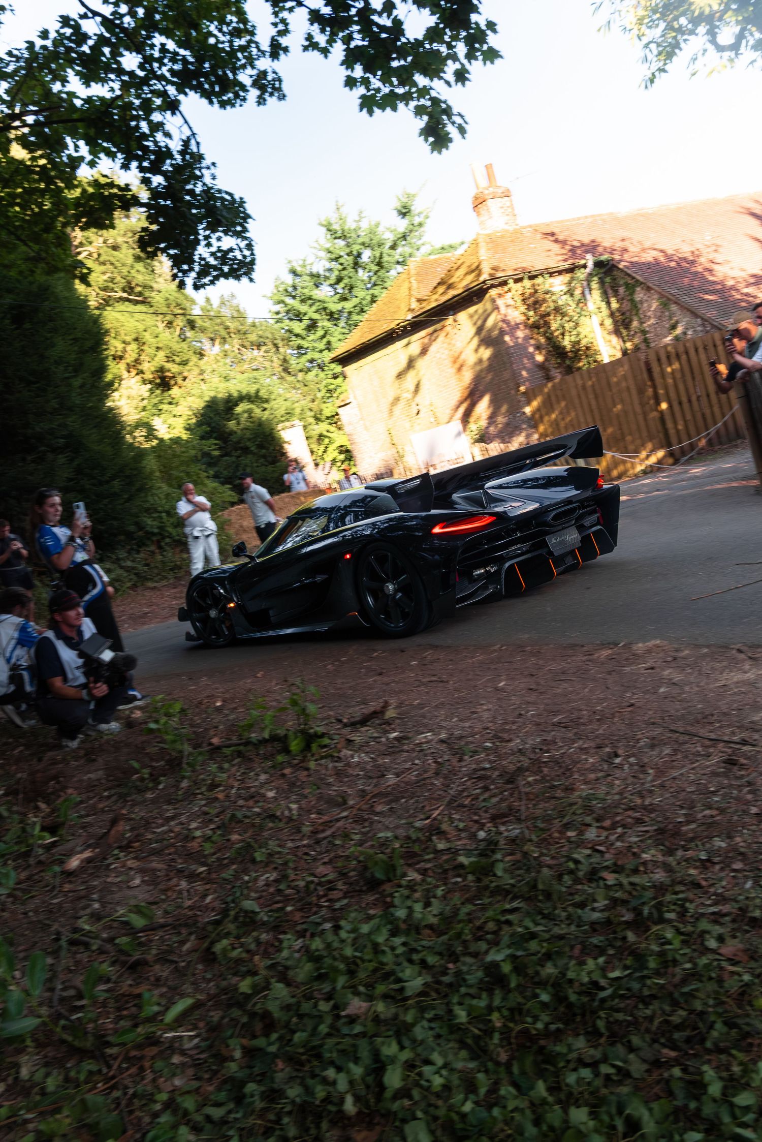 Black supercar racing past spectators on a tree-lined track at Goodwood Festival of Speed.