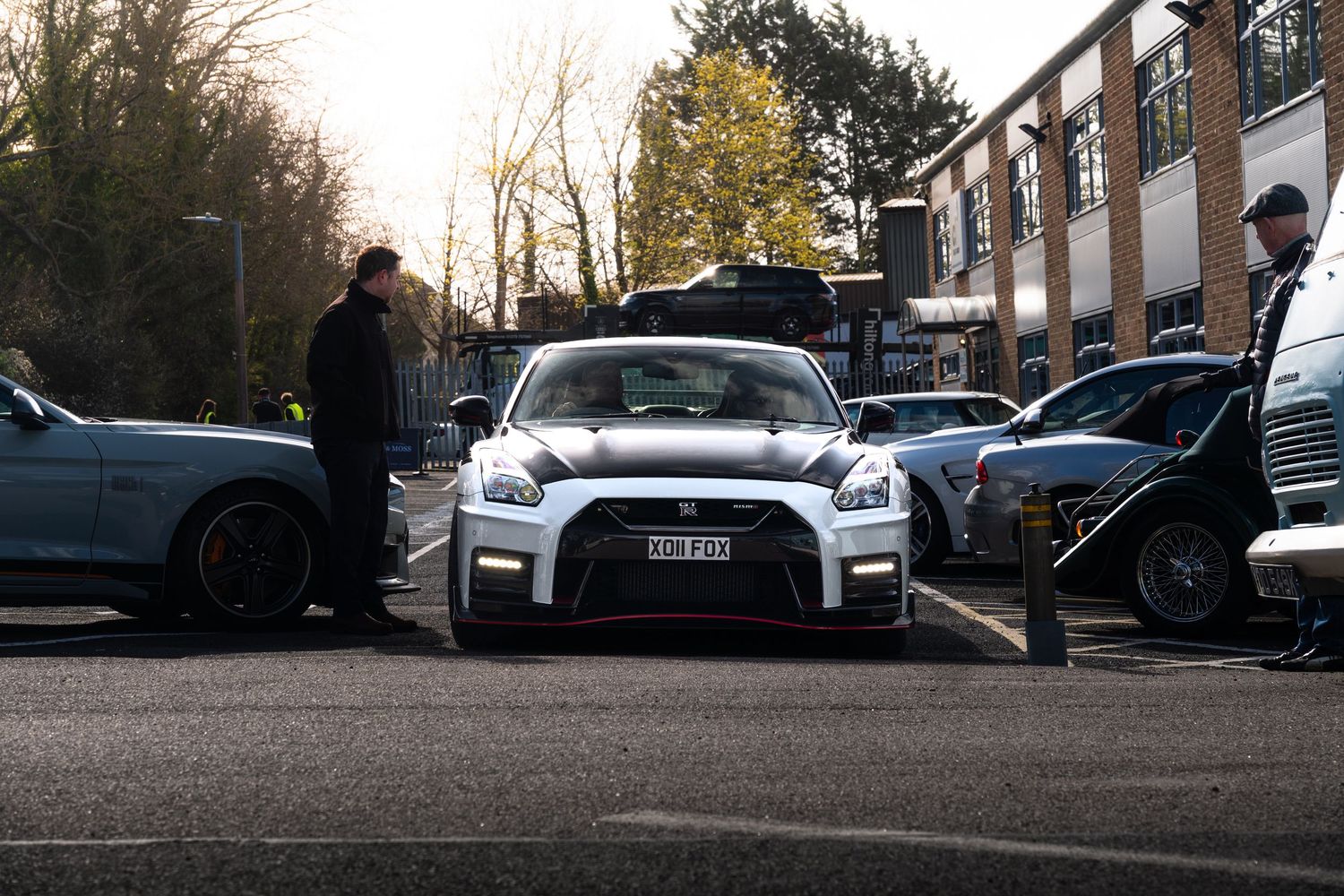 White Nissan GT-R Nismo surrounded by luxury cars at an outdoor automotive gathering on a sunny day.