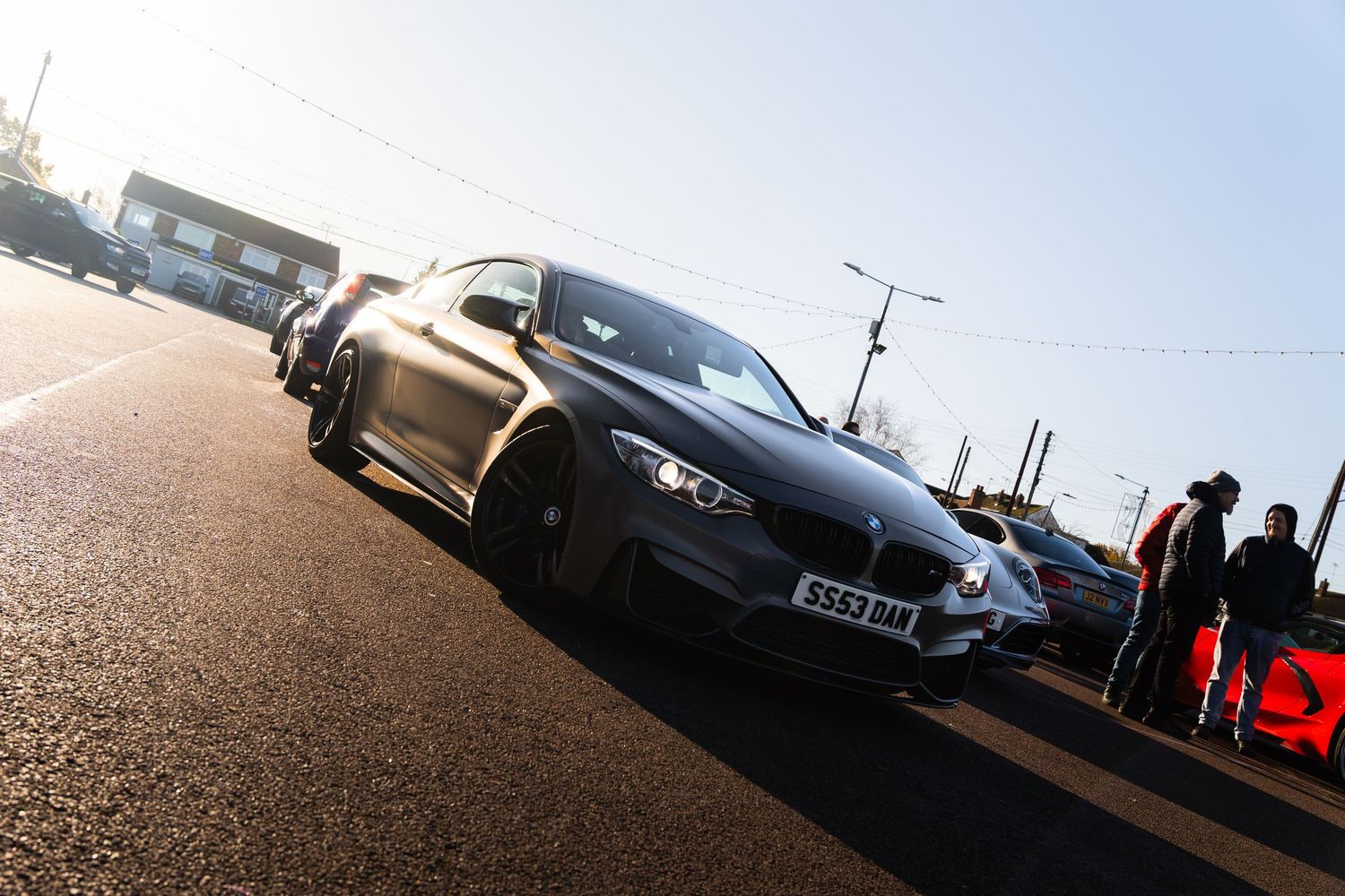 Matte grey BMW M4 coupe parked on a sunny road at a car meet event.