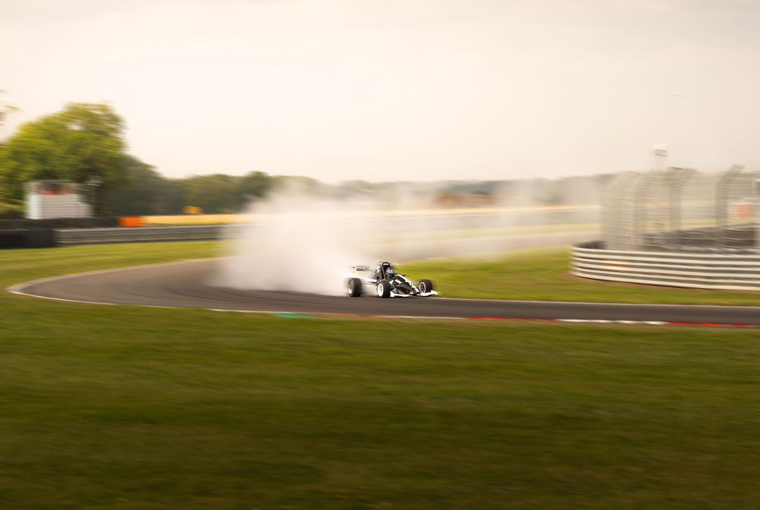 Formula car spinning out on a racing circuit, creating dramatic smoke clouds on a green track.