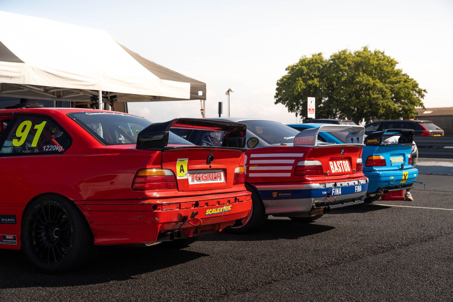 Row of colorful touring cars including red number 91 BMW lined up in racing paddock.