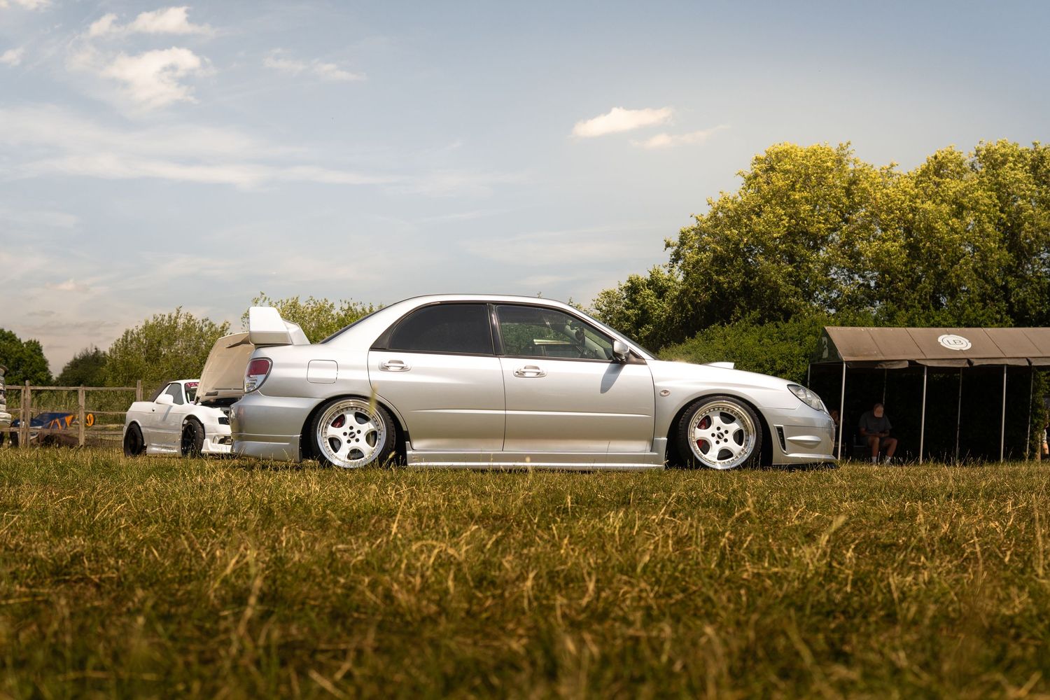 Silver Subaru Impreza WRX sedan on white wheels parked on grass at an outdoor car meet.