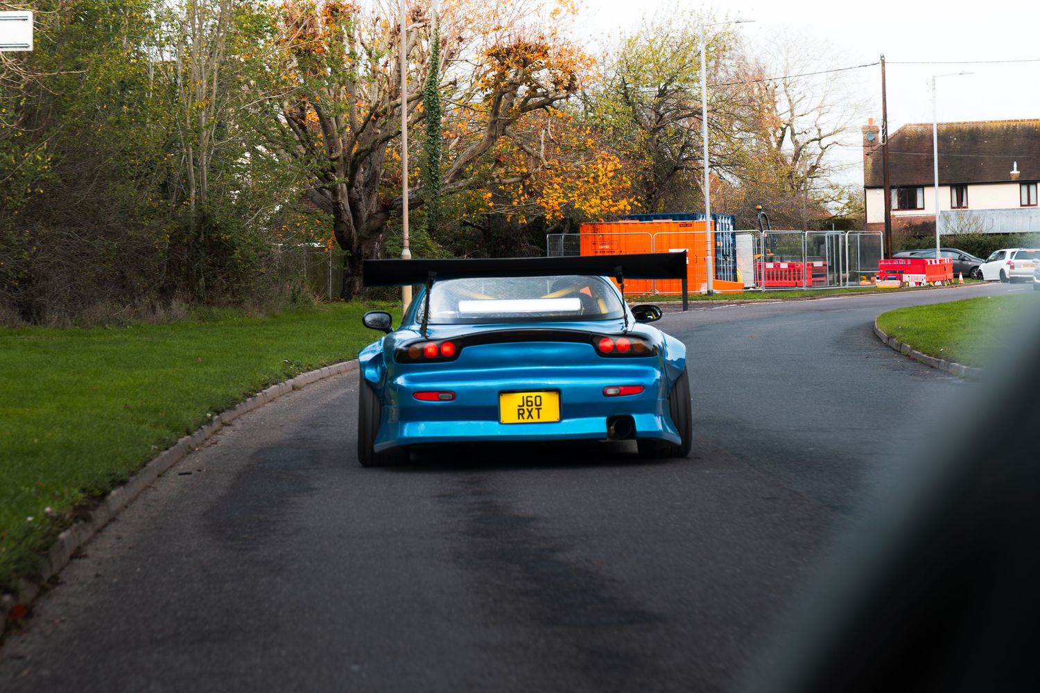 Blue widebody Mazda RX-7 with large rear spoiler driving on a UK road in autumn.