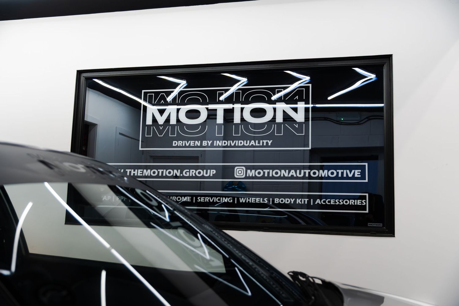 Motion Automotive branded signage displayed above a black car hood in a showroom.