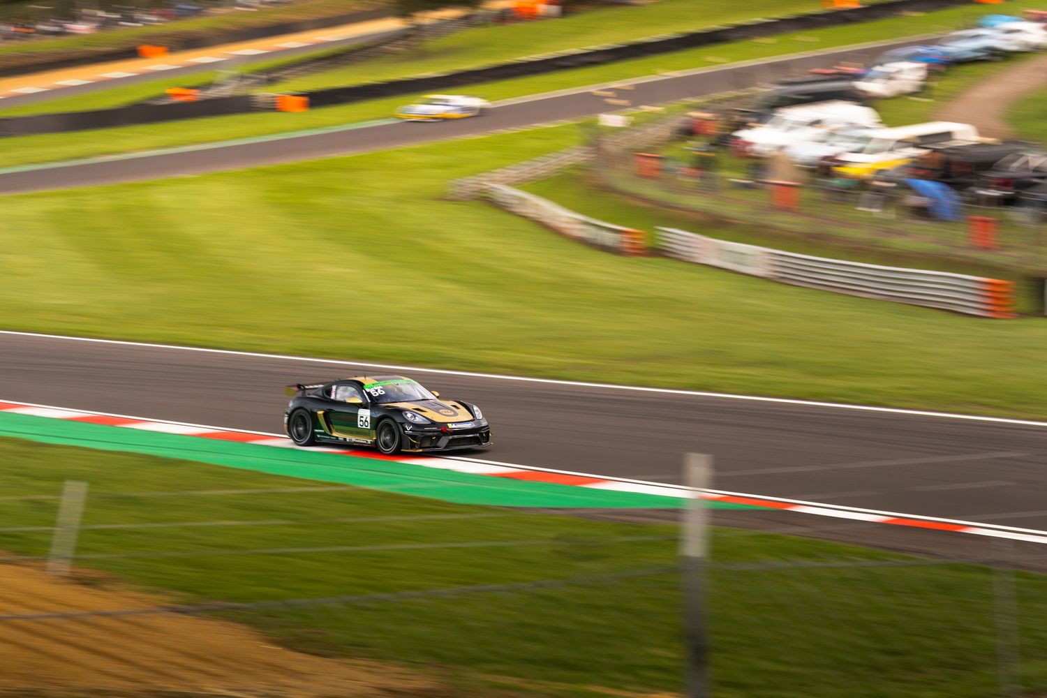 A dark green Porsche GT race car speeds along a circuit track at dusk during a motorsport event.