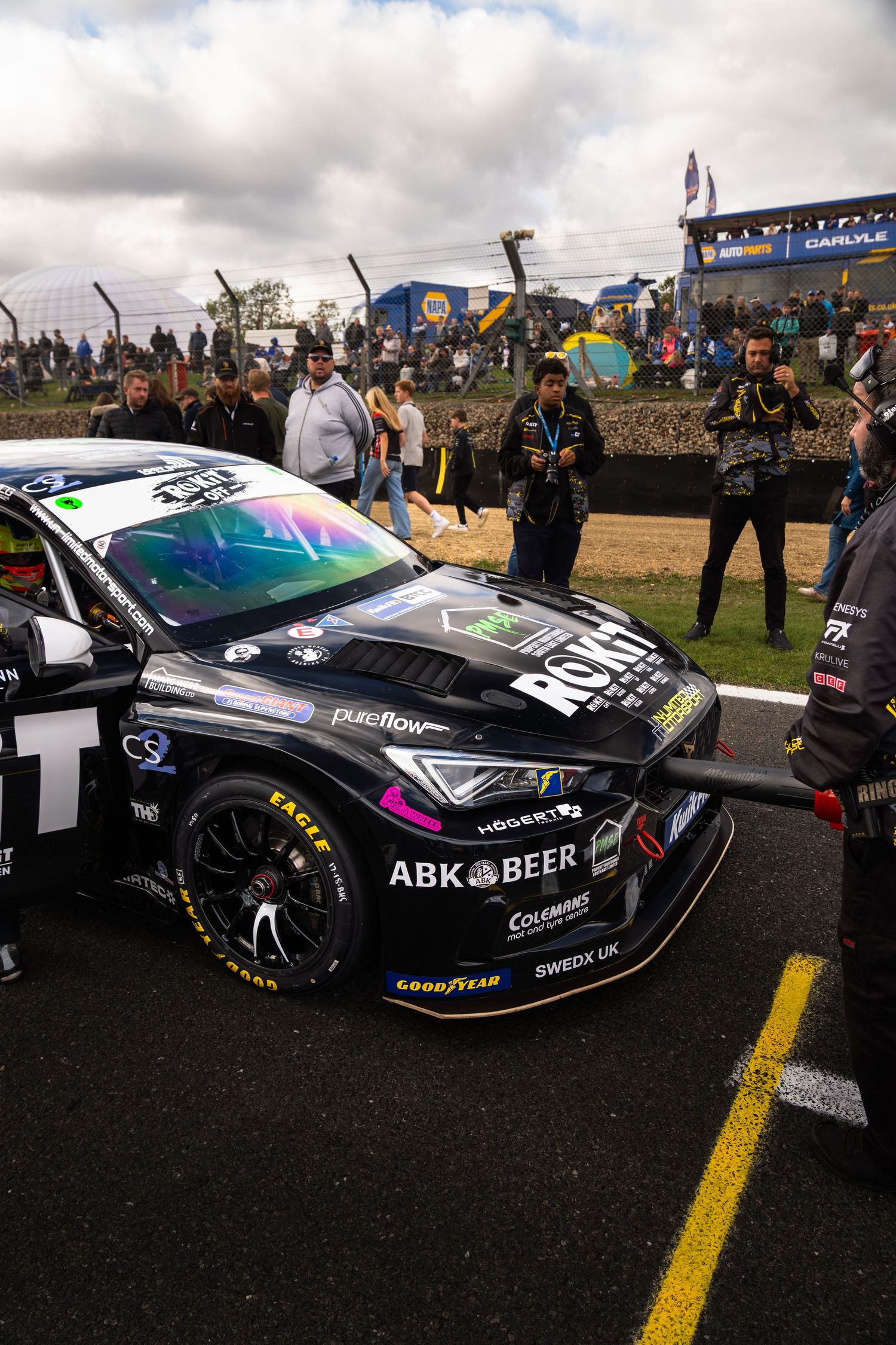Black BTCC Cupra race car with ABK Beer sponsorship on starting grid surrounded by crowd.