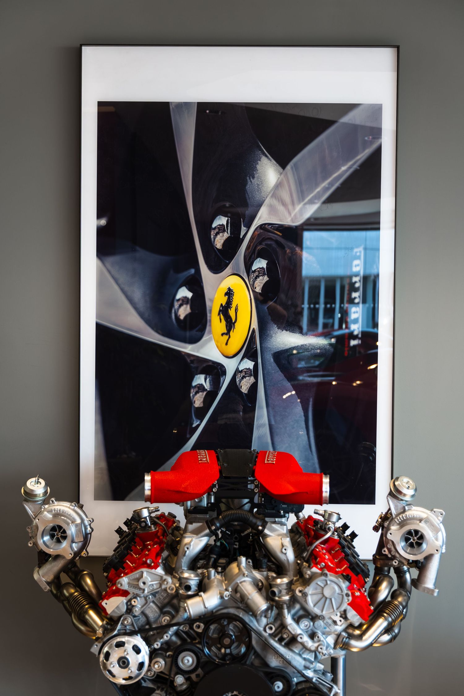 Ferrari twin-turbo V8 engine display with a framed photo of a Ferrari wheel featuring the iconic prancing horse logo.