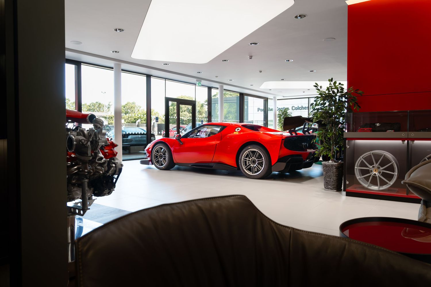 Red Ferrari sports car displayed in a modern luxury car dealership showroom with large windows and clean interior.