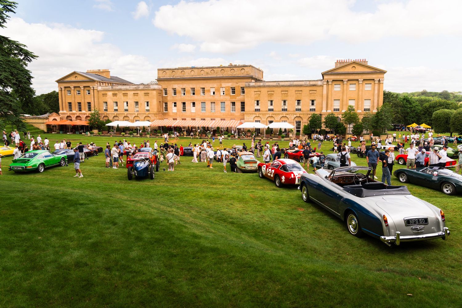 Vintage classic cars displayed on green lawn at elegant English country estate during outdoor concours d'elegance event.