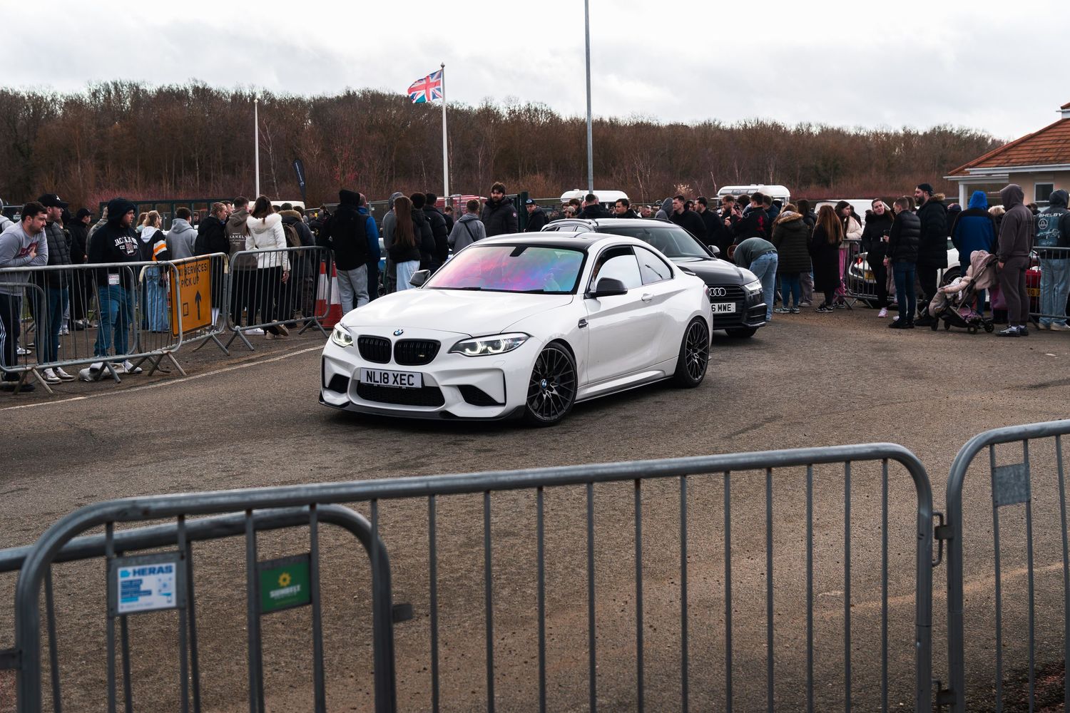 White BMW M2 coupe with iridescent hood at a UK car meet event.