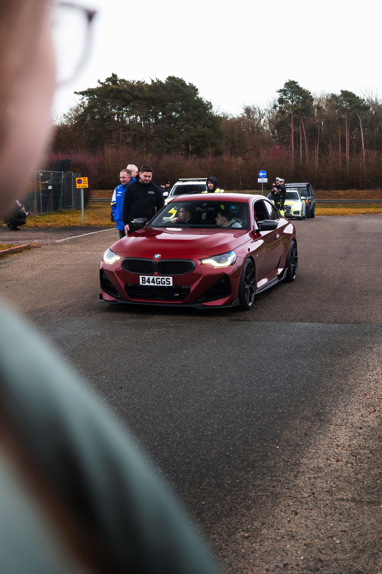 Red BMW M2 with B44GGS plate on wet track surrounded by spectators at UK motorsport event in winter.