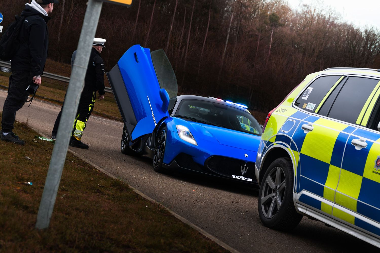 Blue Lamborghini with scissor doors open pulled over by UK Roads Policing Unit on roadside in winter.