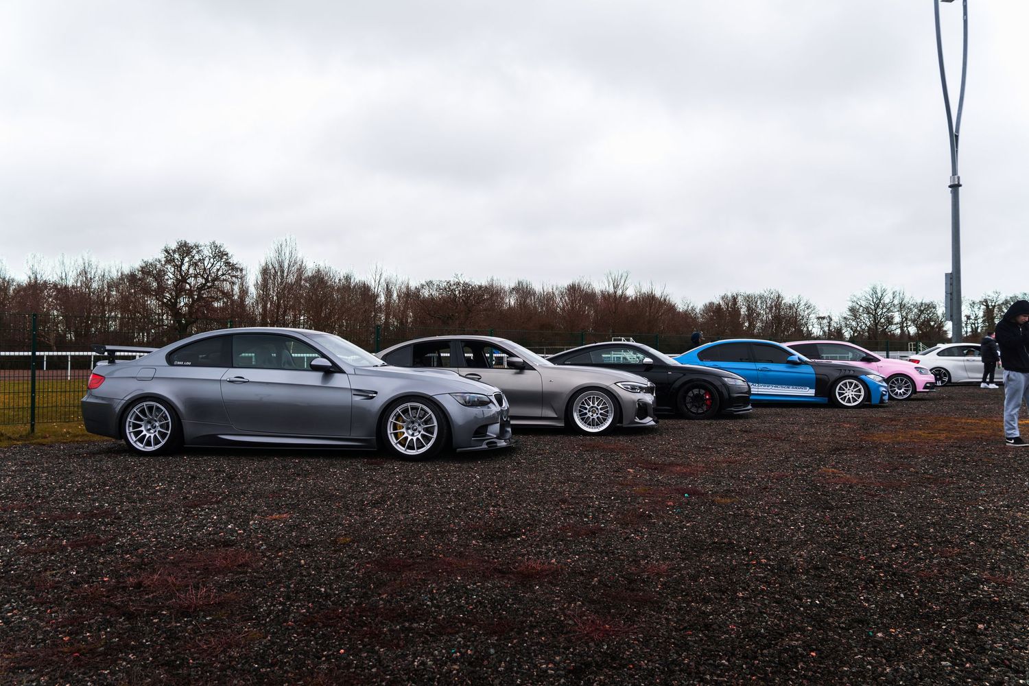 Row of modified performance cars parked on gravel at an outdoor car meet.