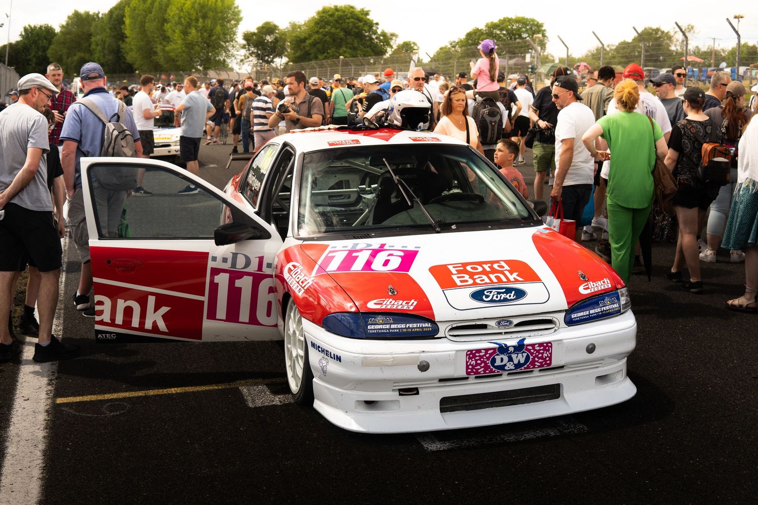 A Ford number 116 touring car surrounded by crowds at a motorsport event.