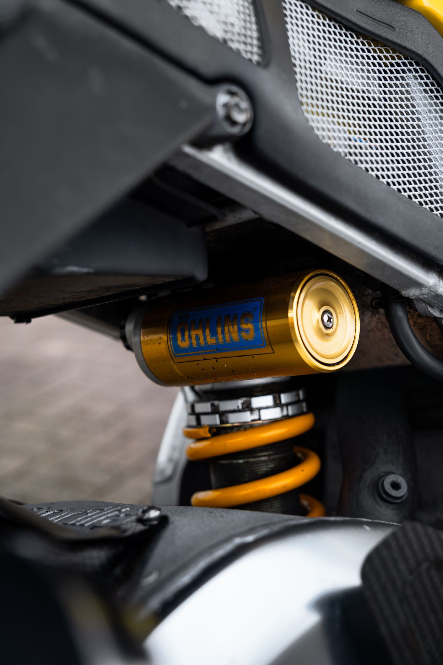 Gold Ohlins rear shock absorber on yellow Aprilia racing motorcycle close-up detail.
