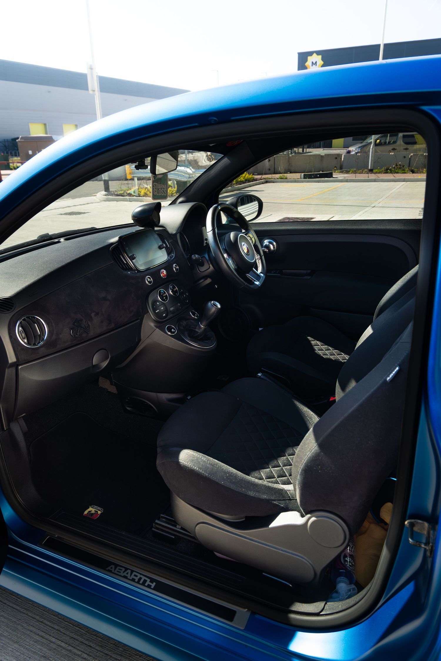 Blue Abarth 500 interior view showing black sport seats, Abarth steering wheel, and right-hand drive layout.