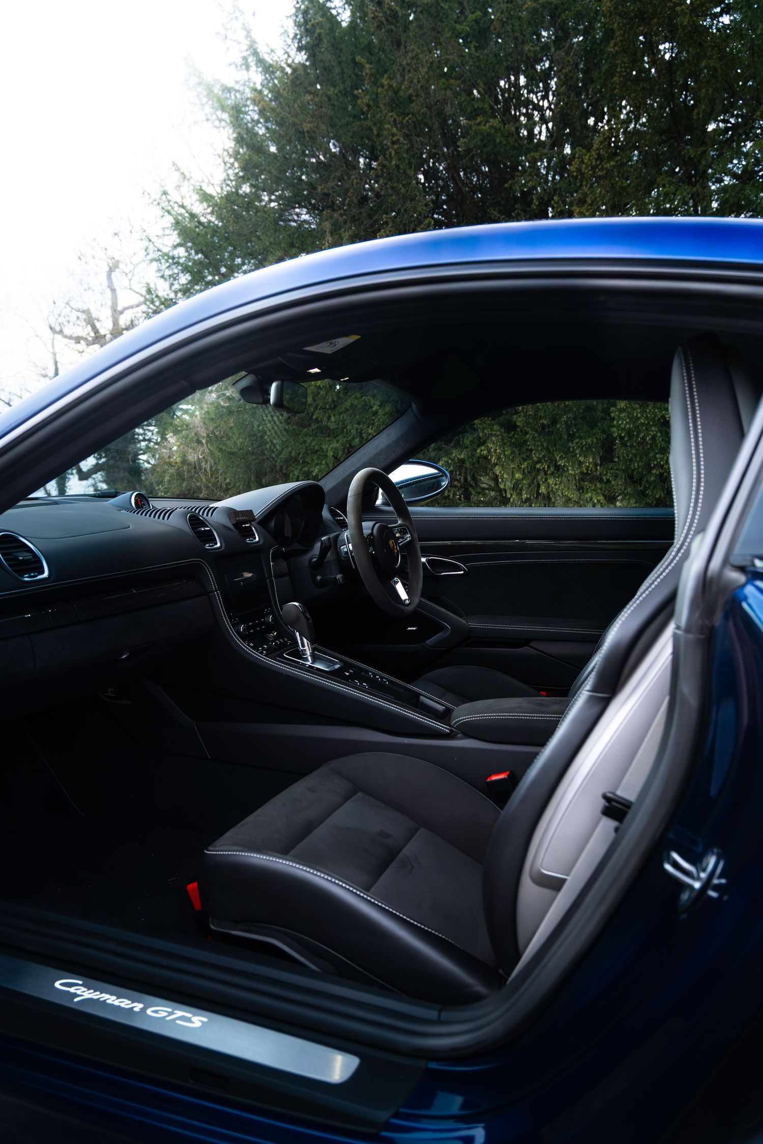 Blue Porsche Cayman GTS interior view showing black sport seats and dashboard through open driver door.