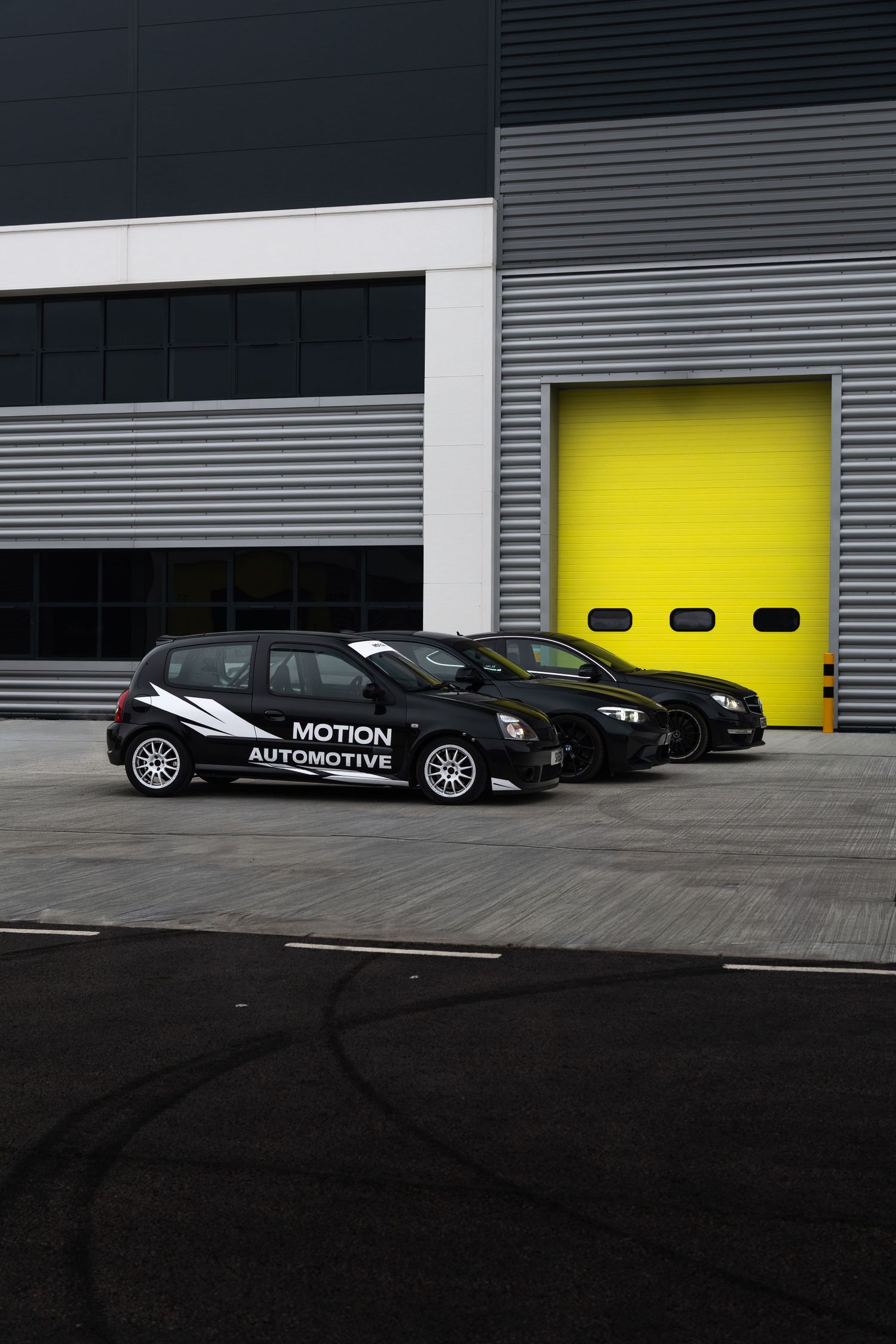 Three black cars parked outside Motion Automotive workshop with yellow roller shutter garage door.