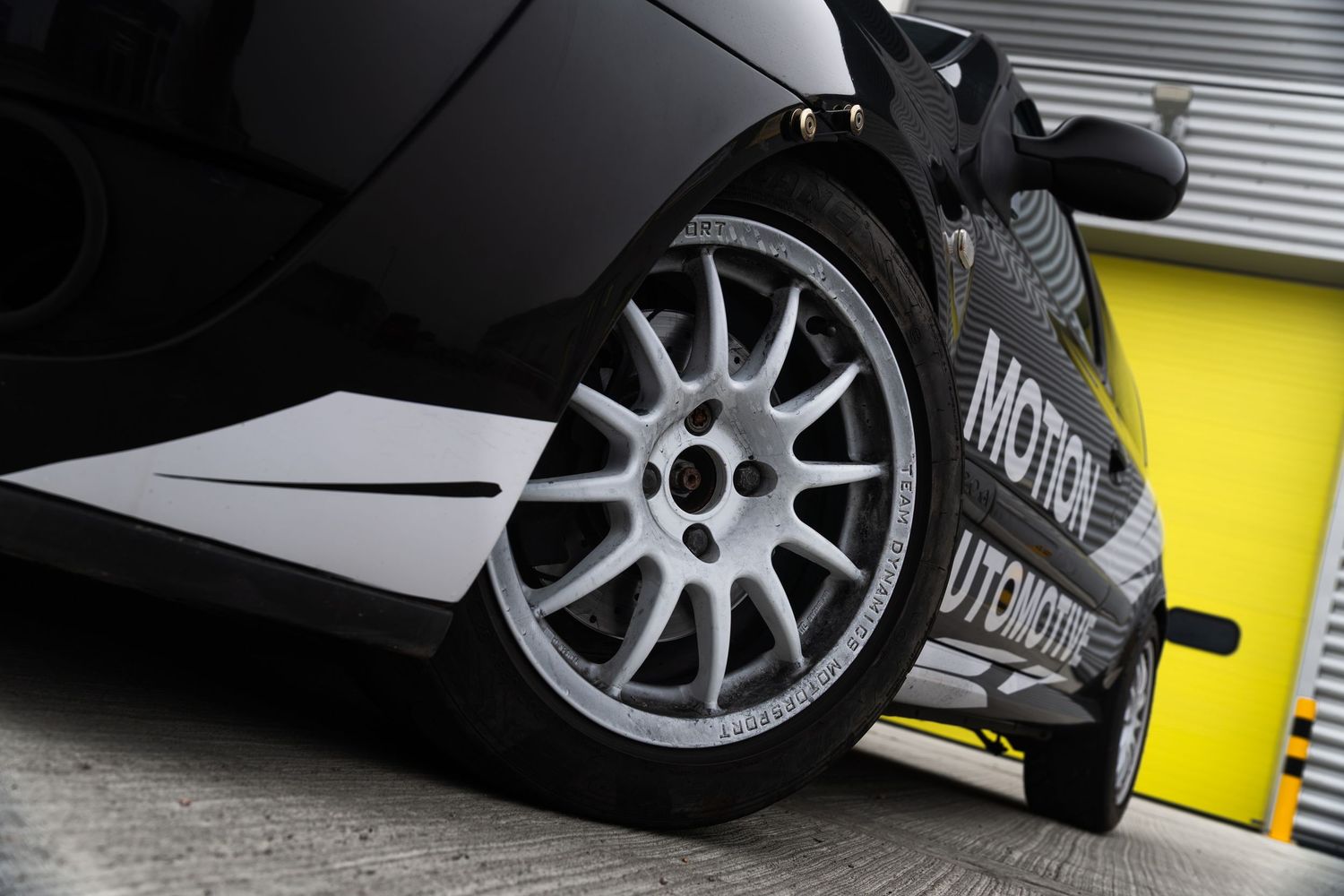 Close-up of white alloy wheel on black Motion Automotive racing Renault Clio with wide performance tires.