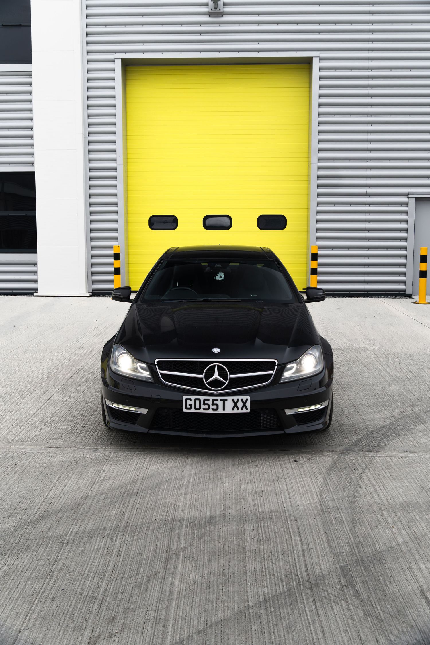 Front view of black Mercedes-AMG C63 coupe parked directly in front of yellow garage door.