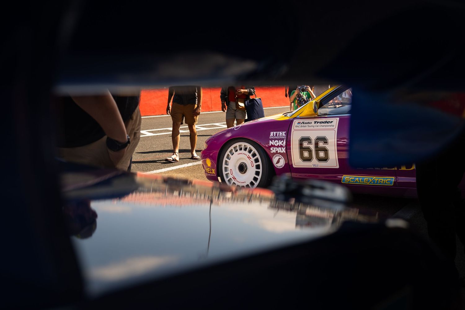 Purple race car number 66 reflected in puddle at motorsport paddock area.