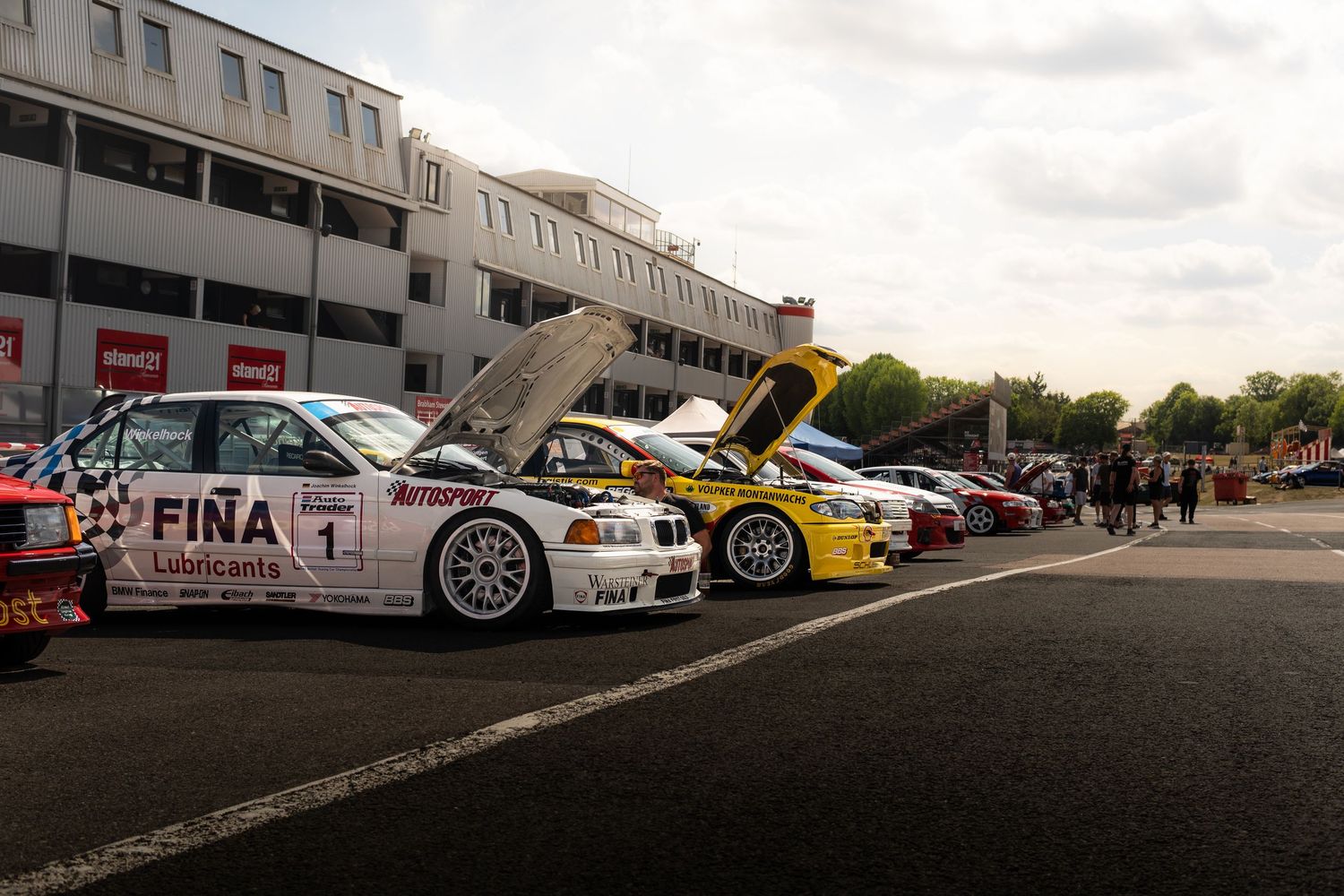 Row of touring cars including white Fina BMW number 1 at motorsport paddock display.