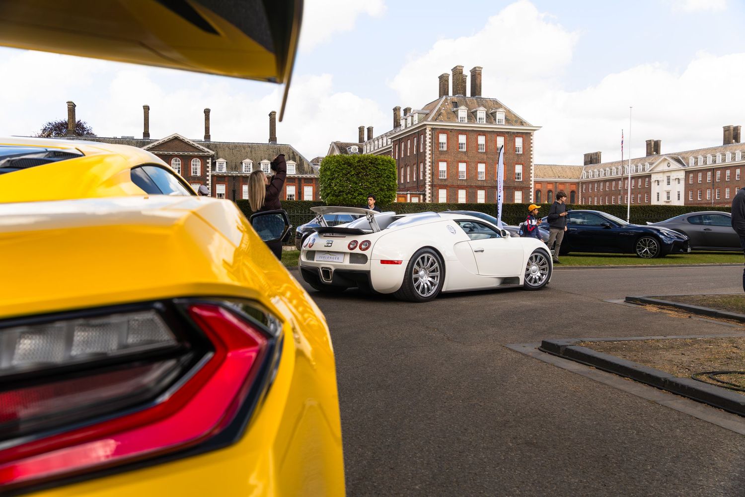 Yellow and white supercars including a Bugatti Veyron parked at a prestigious outdoor automotive event.