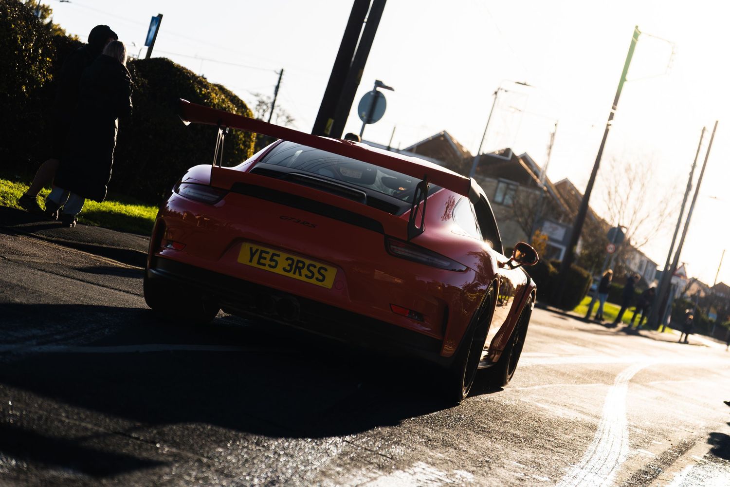 Orange Porsche 911 GT3 RS navigating a roundabout on a sunny day in a residential area.