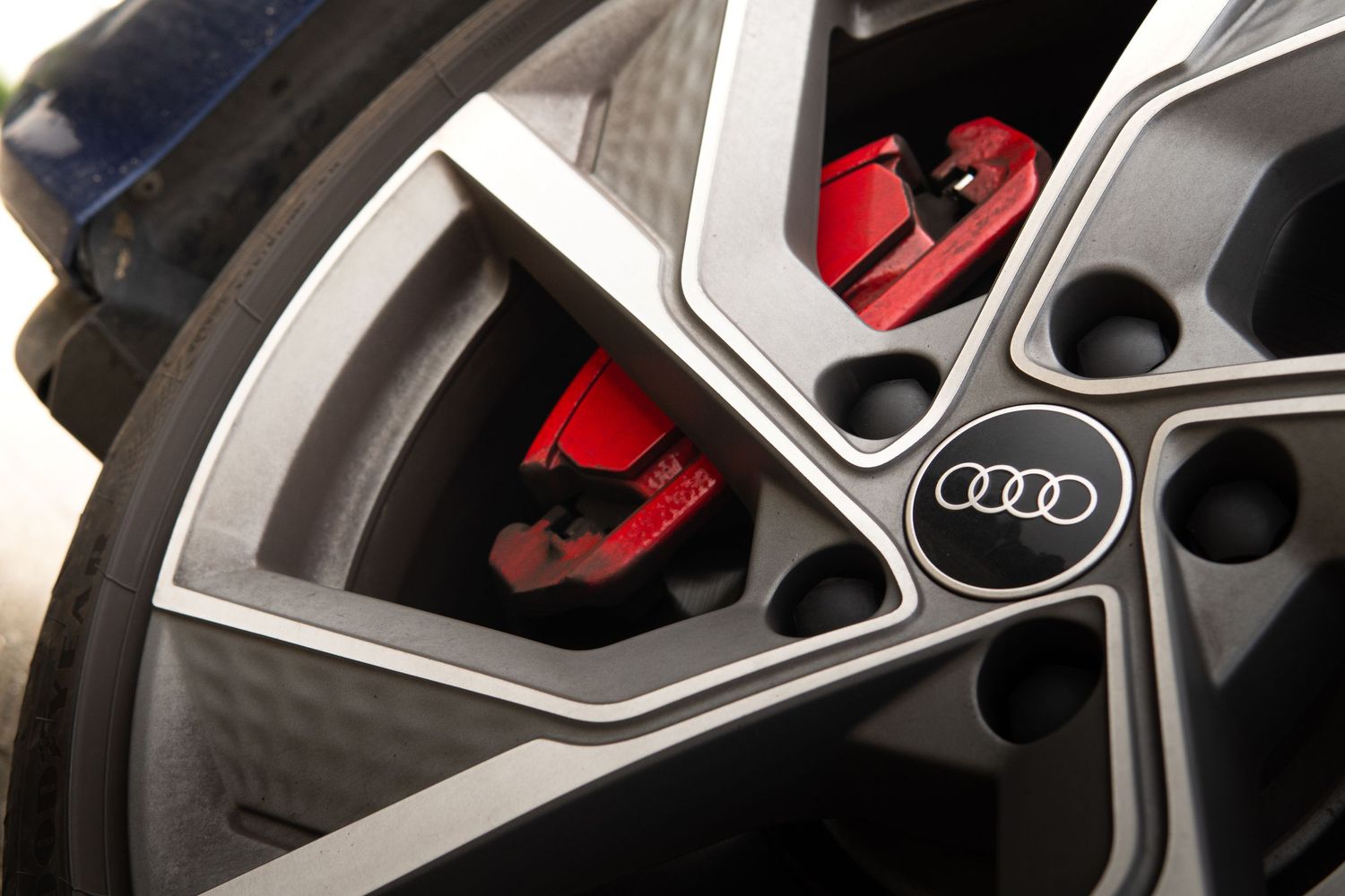 Close-up of Audi alloy wheel with red brake calipers and four-ring logo badge.