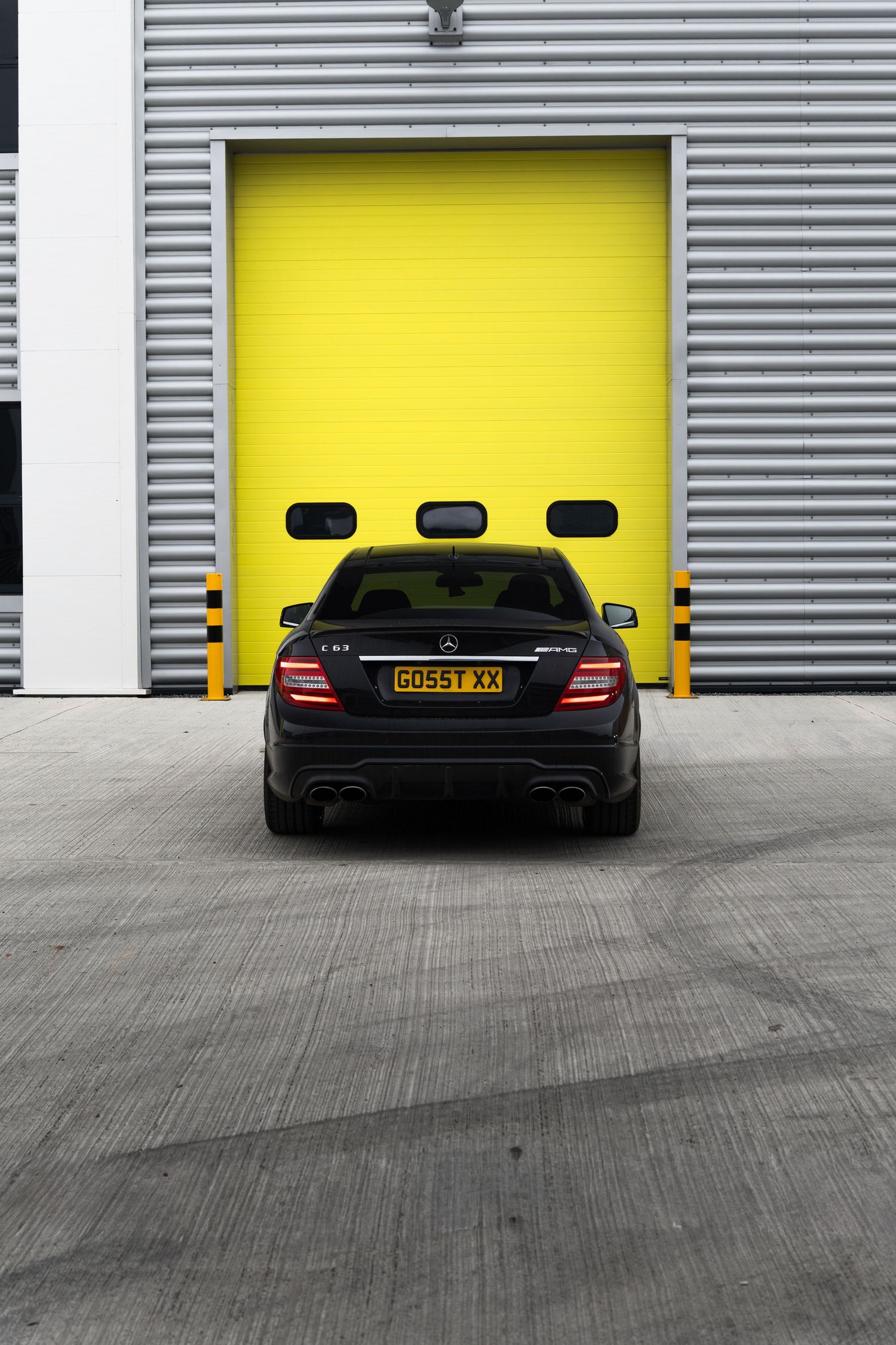 Rear view of a black Mercedes-Benz C63 AMG coupe parked in front of a yellow roller door.