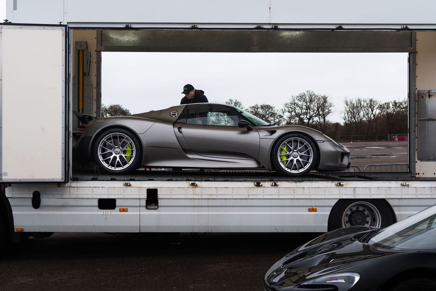 Silver Porsche 918 Spyder supercar being unloaded from transport truck.