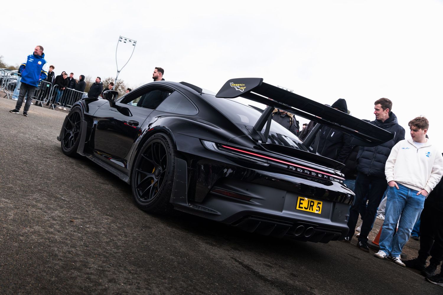 Black Porsche 911 GT3 RS race car with large rear wing at a motorsport event.