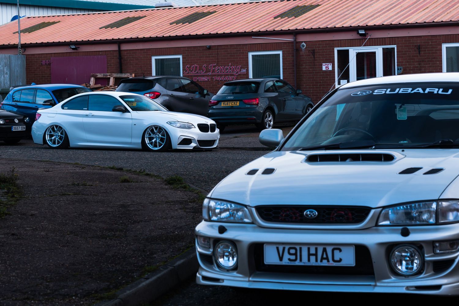 White Subaru Impreza WRX STI and BMW coupe parked near a red brick building.