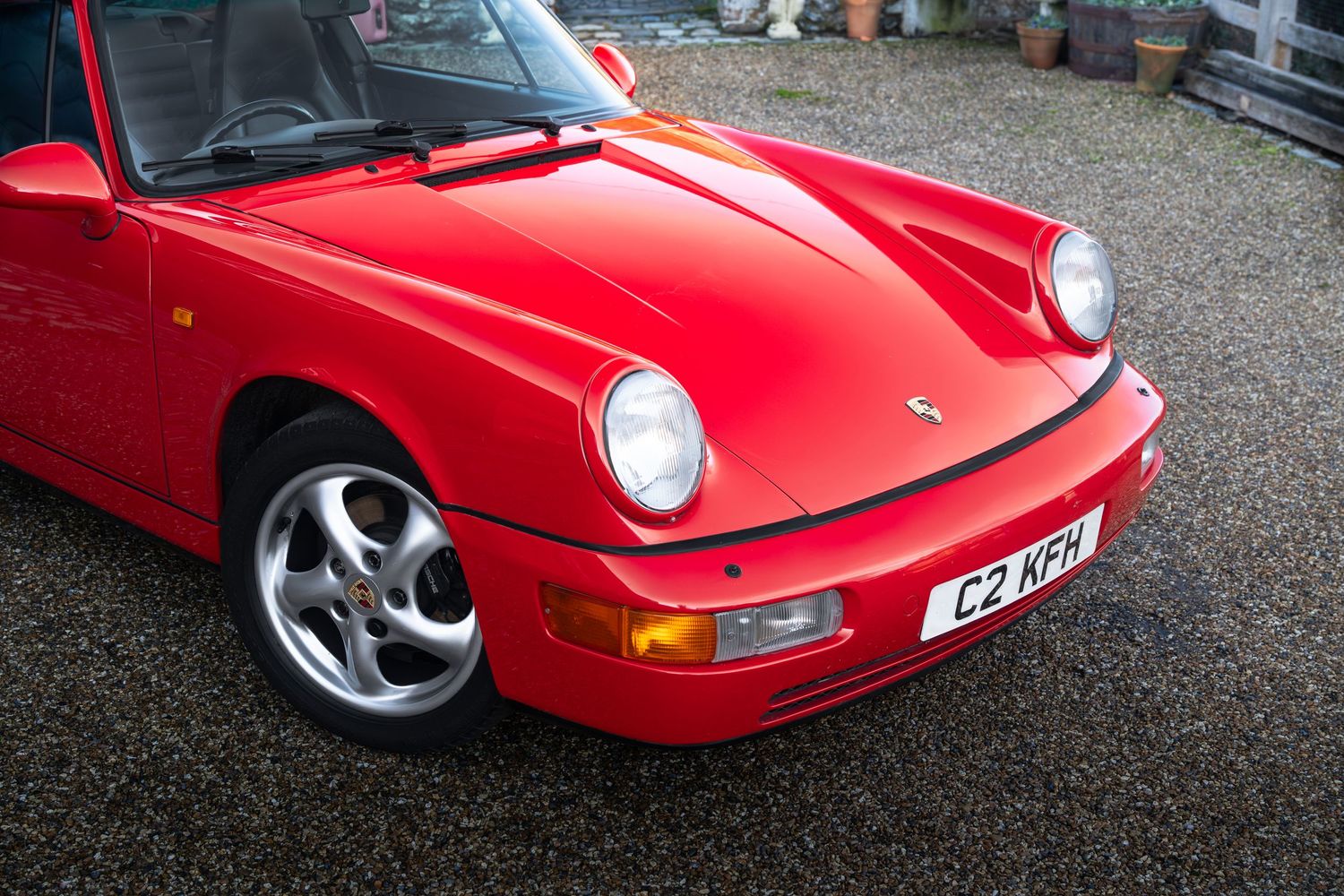 Front detail of a Guards Red Porsche 911 Carrera with UK registration plate C2 KFH on gravel driveway.