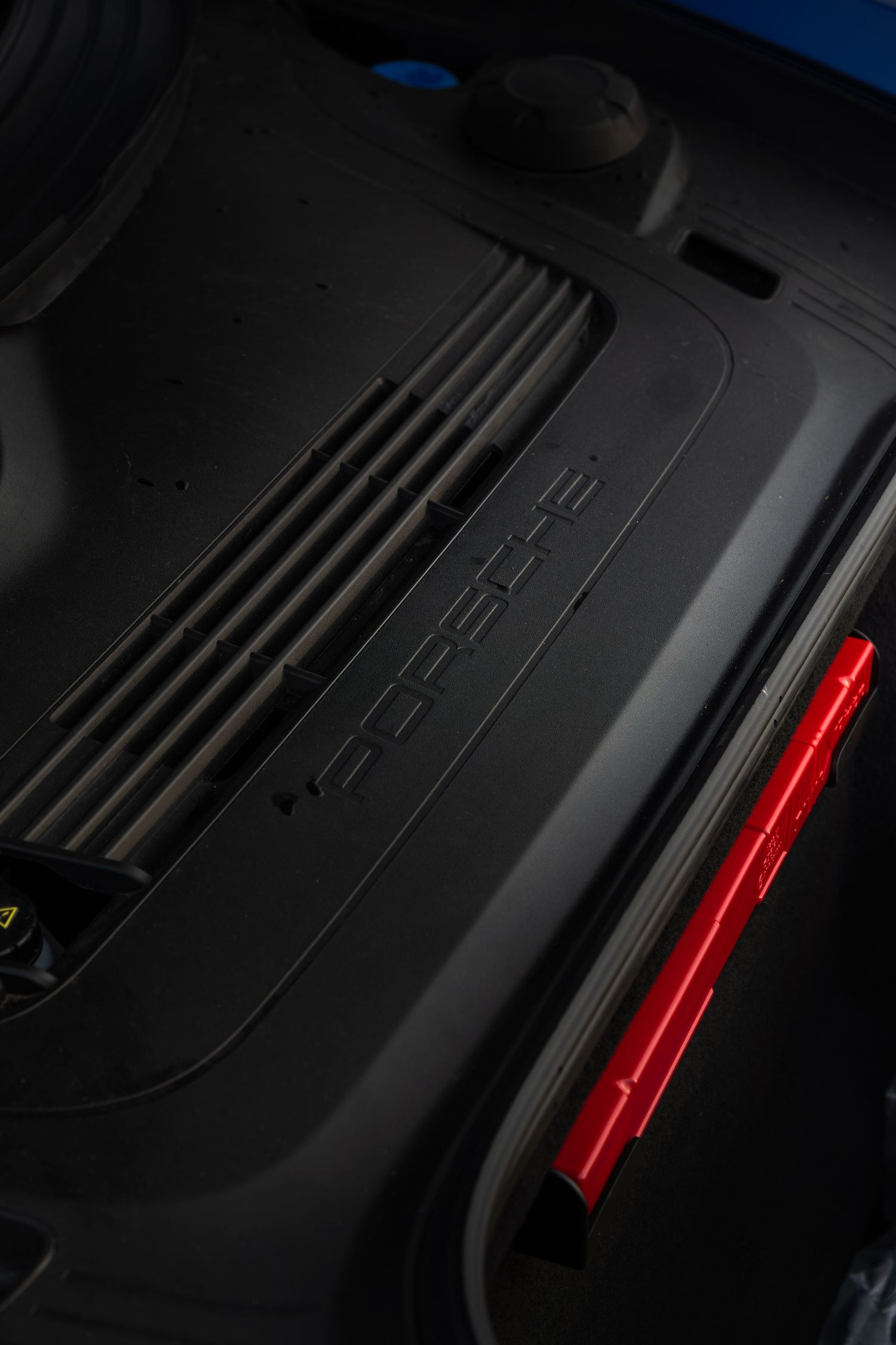 Close-up of Porsche engine cover with embossed logo and red accent detail visible.