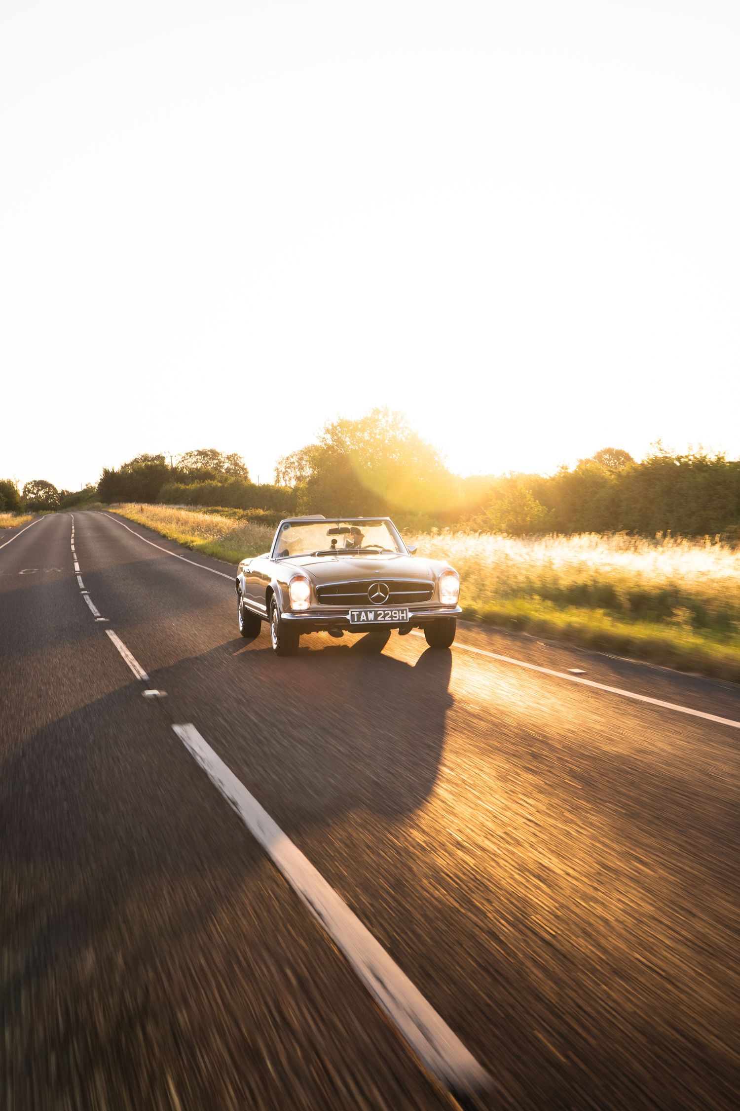 Classic Mercedes-Benz convertible driving on a rural road at golden sunset hour.