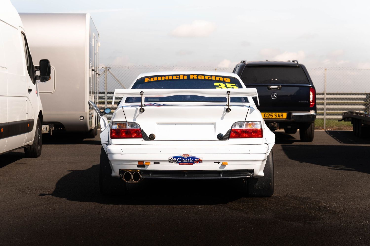 White Eurotek Racing touring car rear view with large spoiler in motorsport paddock.