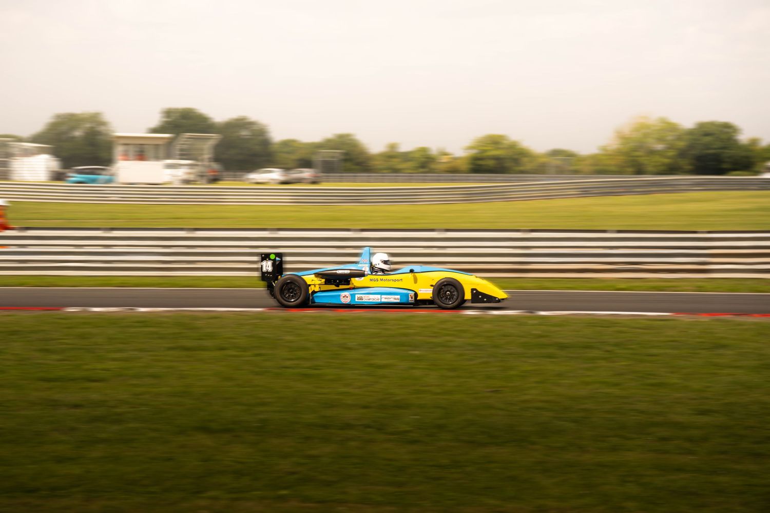 Yellow and blue formula racing car speeding around a motorsport circuit track.