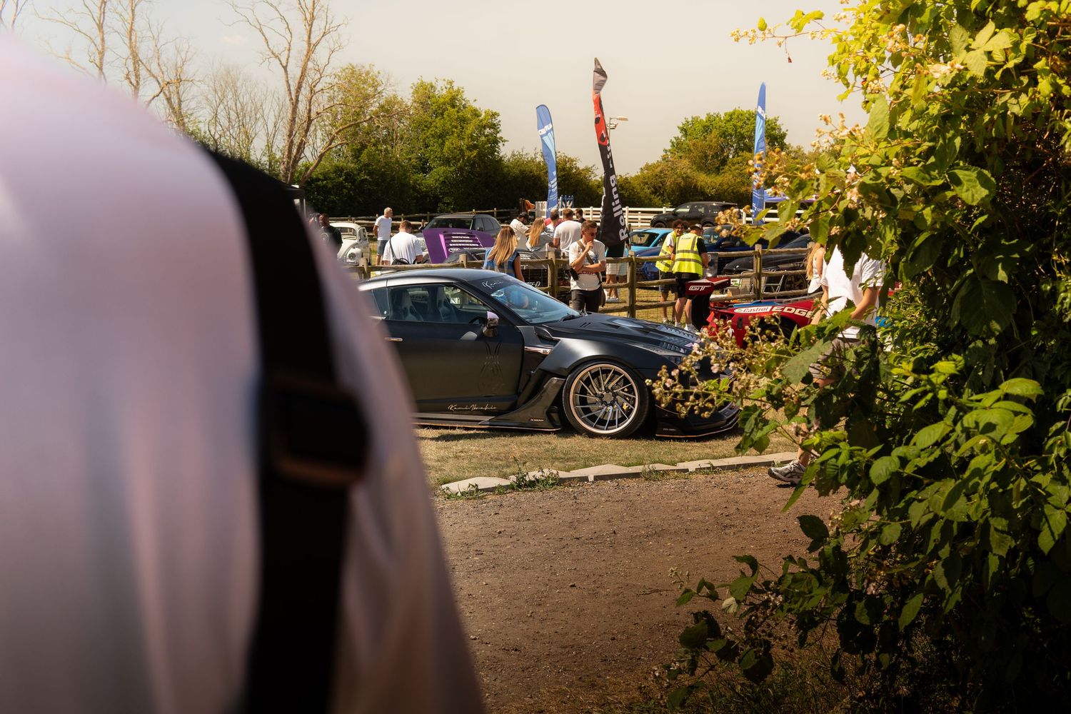 Dark modified BMW at busy outdoor car show event with crowd of spectators.