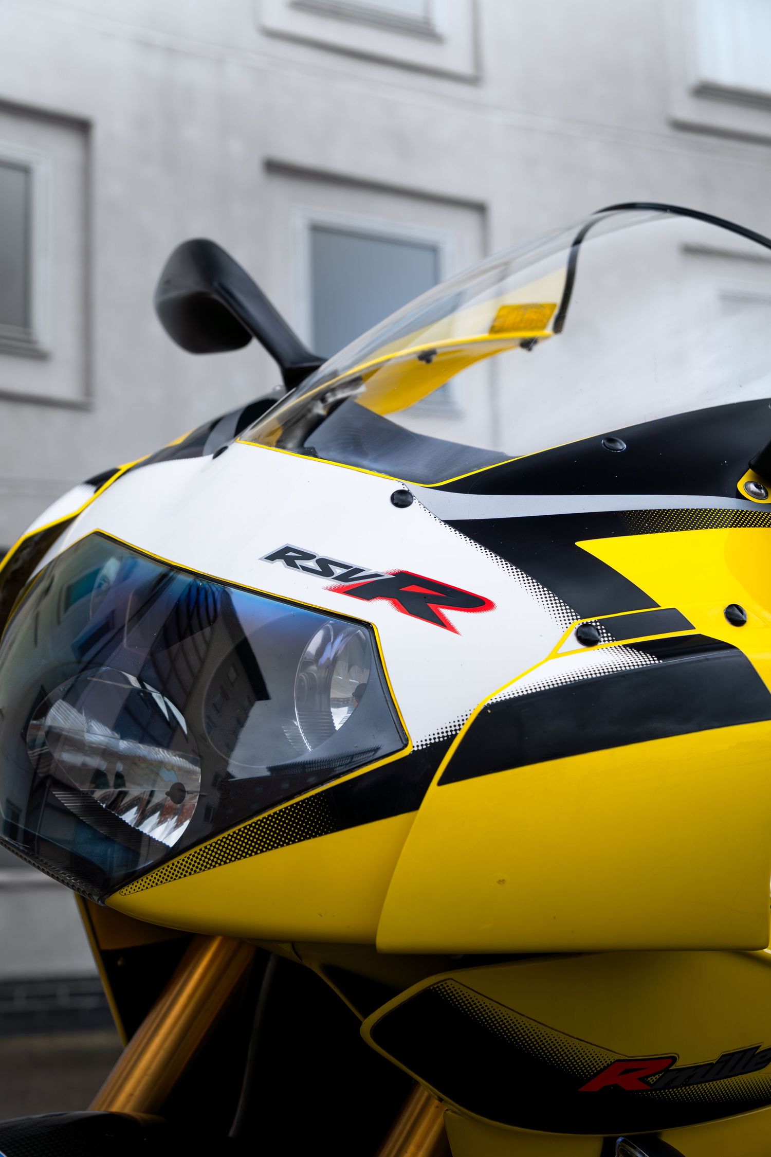 Close-up of yellow Aprilia RSV-R front fairing showing the RSV-R logo, headlight, and carbon fiber details.