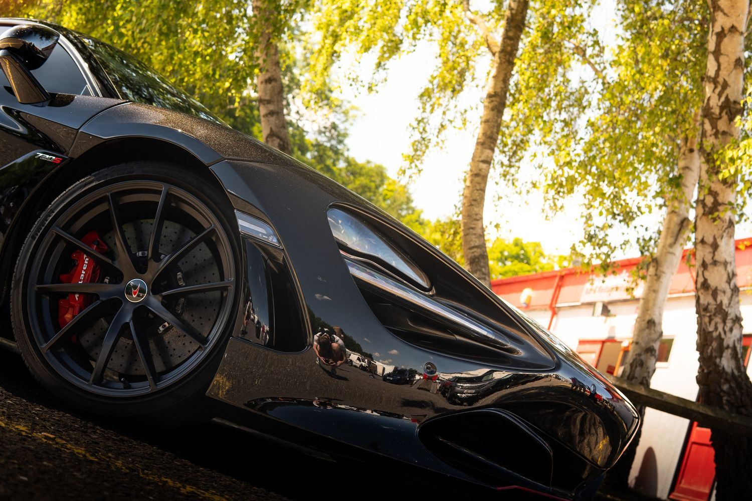 Sleek black McLaren supercar parked near birch trees with red brake calipers visible.