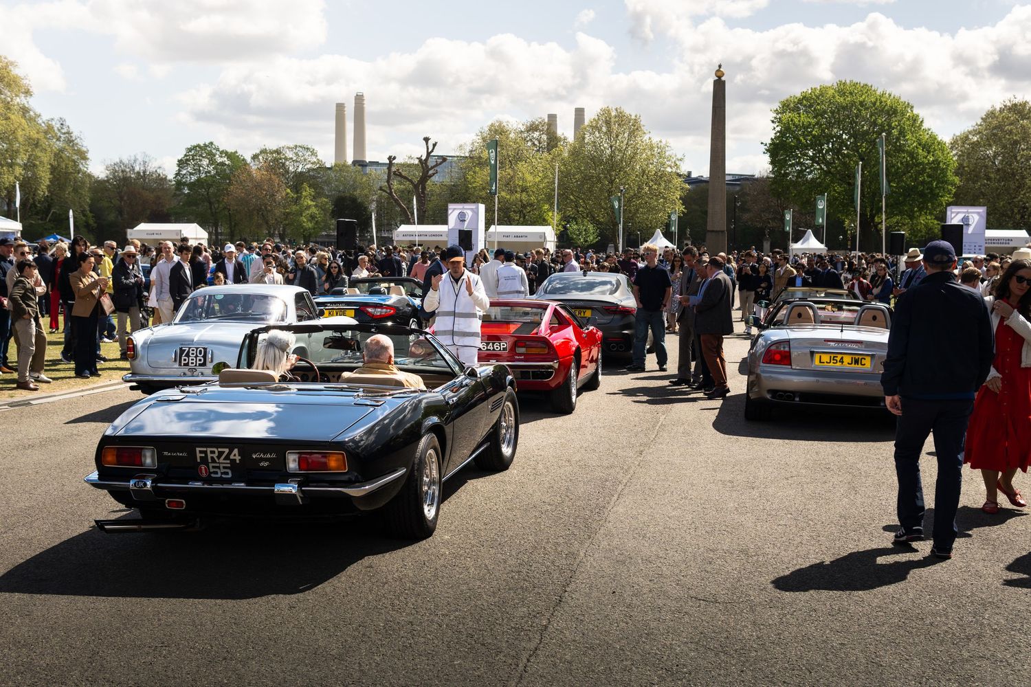 Row of classic convertible sports cars lined up at an outdoor automotive show near an obelisk monument.