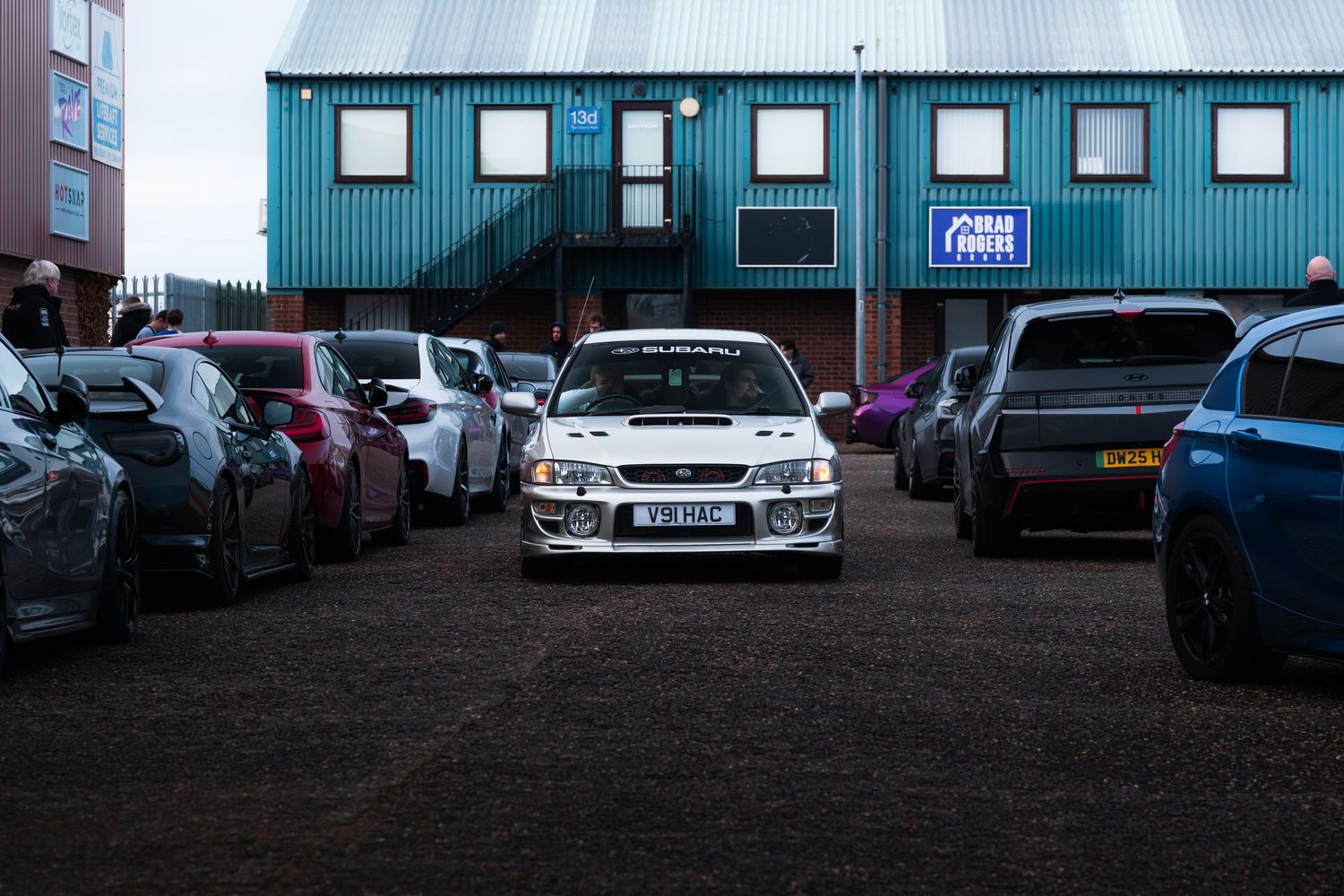 White Subaru Impreza WRX STI centered among rows of parked cars at an outdoor car meet.