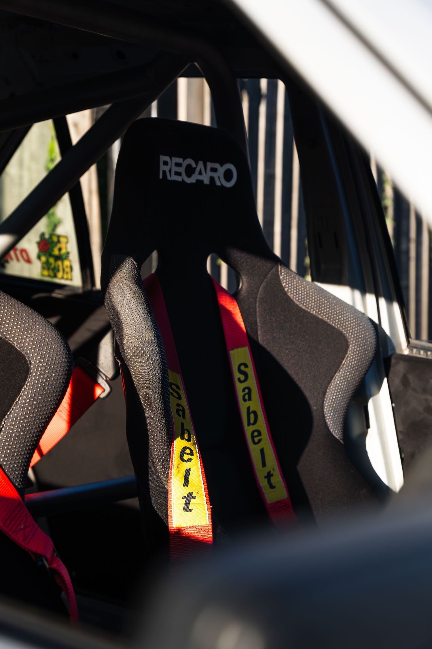 Recaro racing bucket seat with Sabelt harness inside a track-prepared car with roll cage.